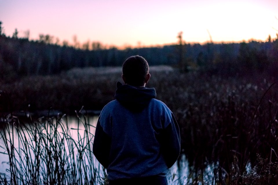 man wearing black and grey hoodie standing near lake