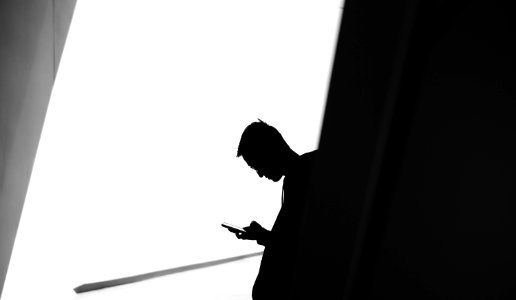 person using phone leaning on wall in silhouette photography photo