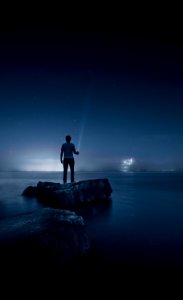 man holding flashlight standing on rock