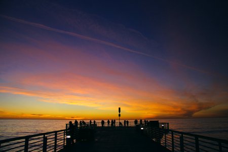 silhouette of people on dock near body of water during golden hour photo