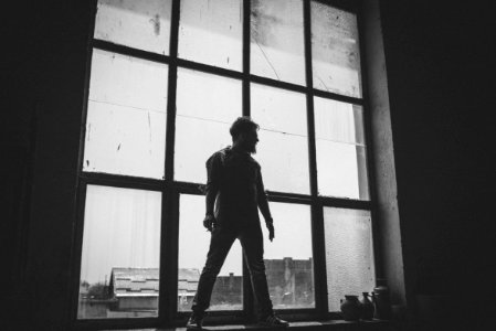man standing against the glass window grayscale photography photo