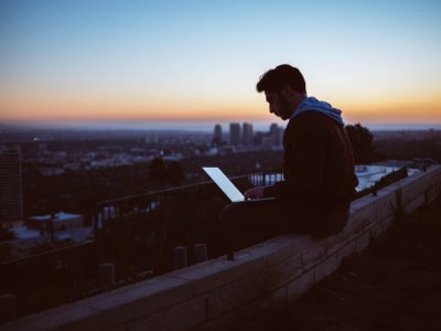 man sitting on concrete brick with opened laptop on his lap photo