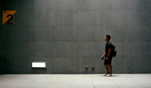 man in black top carrying backpack standing near wall