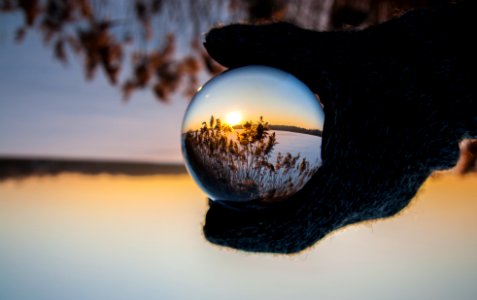 person wearing black gloves holding glass ball reflecting body of water with sunlight photo
