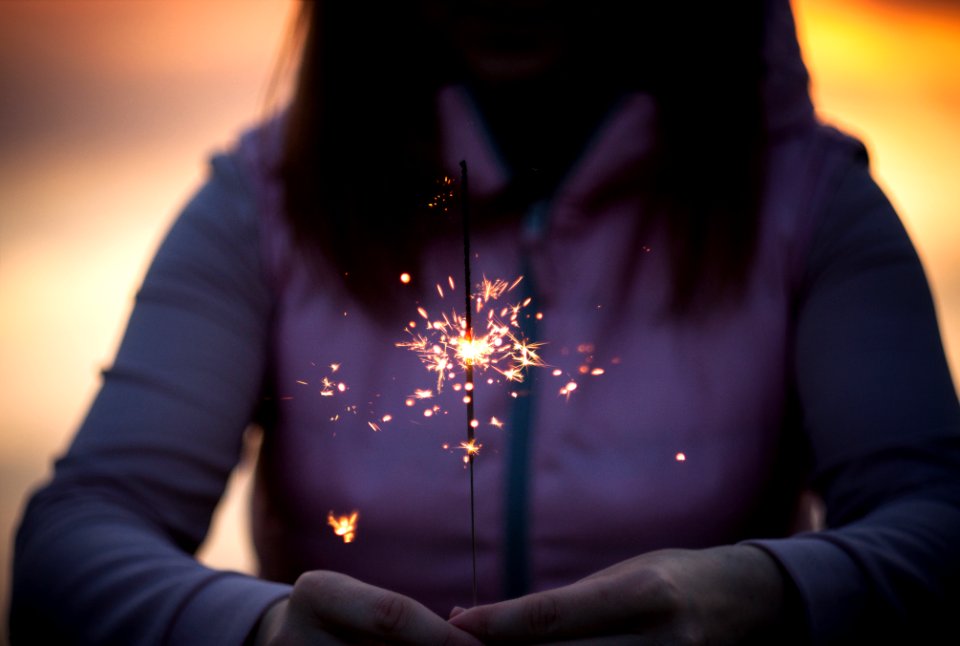A woman in a hoodie holds a lit sparkler in her hands