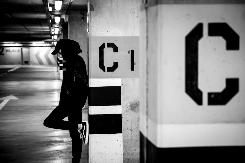 grayscale photo of man leaning on post