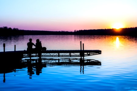 silhouette of two persons sitting on dock photo