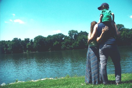 father, mother, and son standing on grass lawn near at body of water during daytime photo