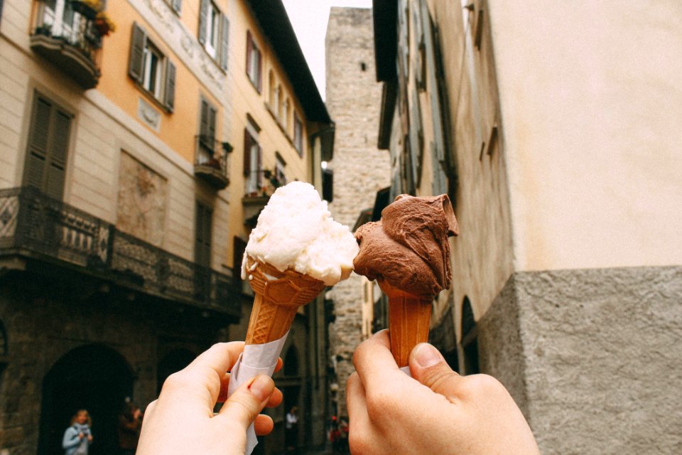 Man and woman hold up chocolate and vanilla ice cream cones in old side street