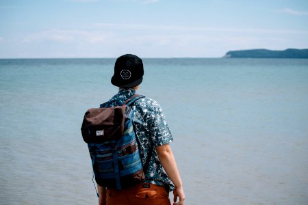 man wearing blue and black backpack standing in front of body of water photo