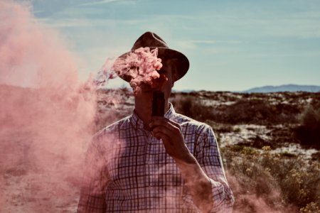 man standing on open field holding device with smoke during daytime photo