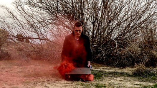 A man opening his suitcase on the ground, as red smoke escapes it.