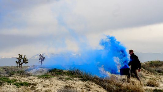 man holding black box with blue smoke walking on grass field during daytime