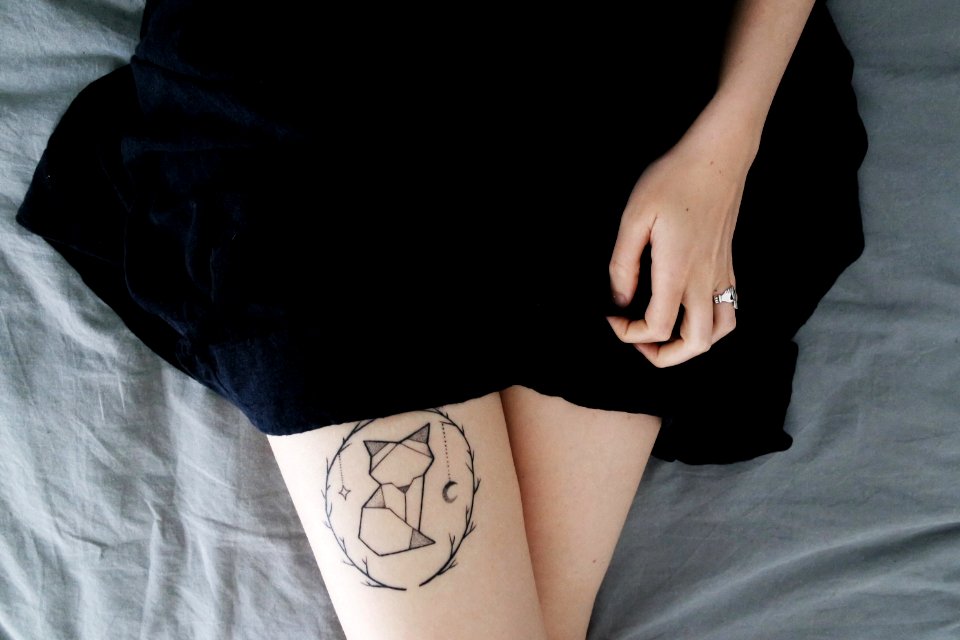 woman lying on bed sowing cat dreamcatcher tattoo on right leg during daytime