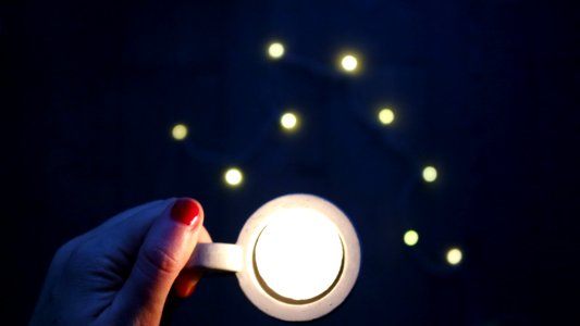 A woman with red fingernail polish holding a cup with a white light in it.