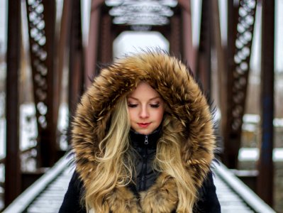 woman wearing brown fur-lined hoodie standing on the bridge during daytime photography photo