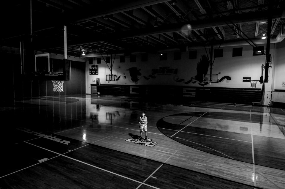 grayscale photo of boy holding ball standing on basketball court