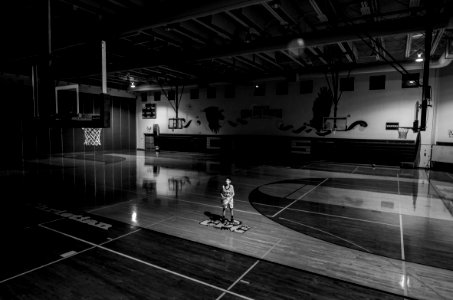 grayscale photo of boy holding ball standing on basketball court photo