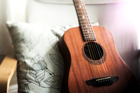 selective focus photo of brown guitar on white pillow photo