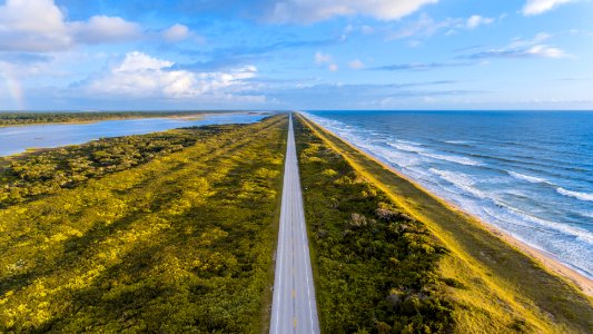aerial view photography of asphalt road in between ocean and trees under cloudy sky photo
