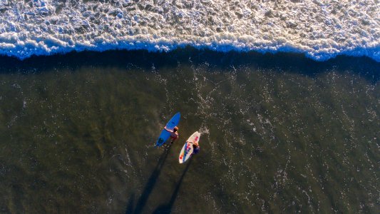 high angle photo of two persons carrying surfboards on seashore photo