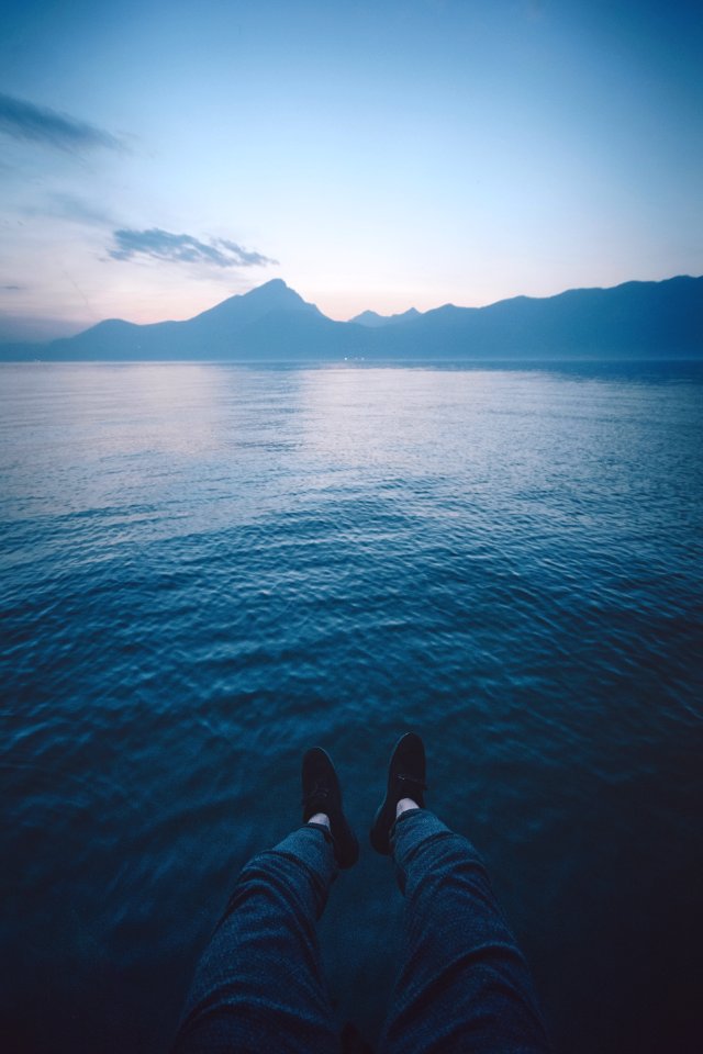 man sitting beside calm body of water