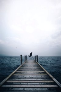 man jumping on brown wooden dock in middle of body of water photo