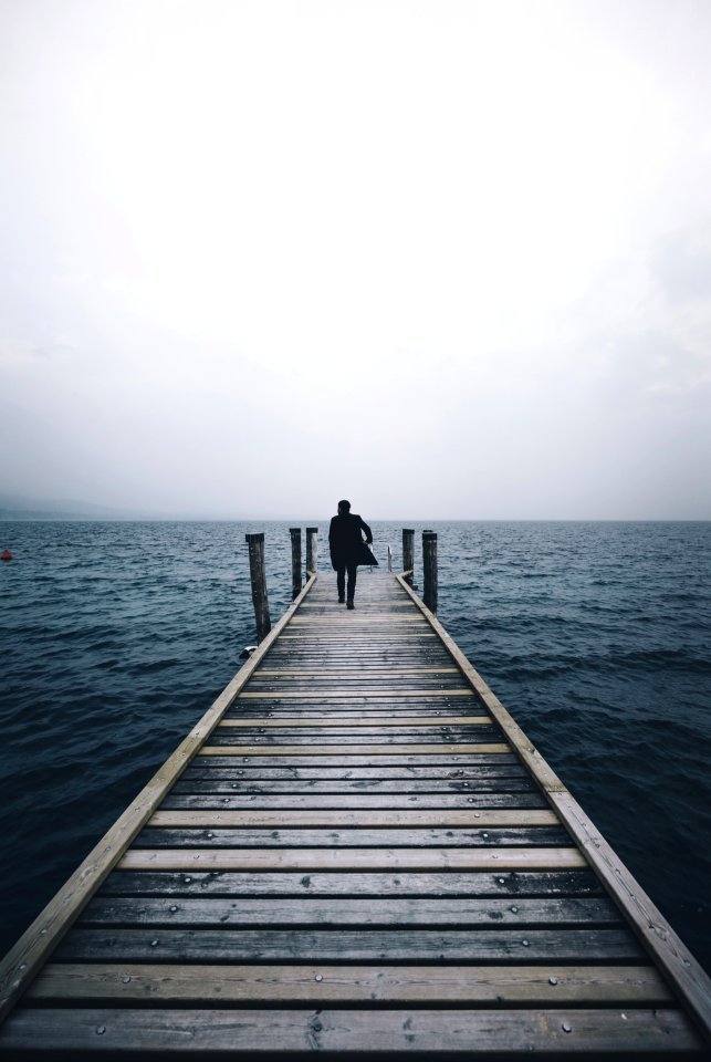 man walking on dock surrounded by ocean during daytime