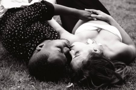 grayscale photo of man and woman facing each other and lying on grass photo