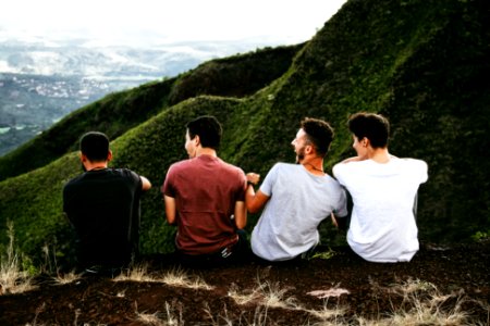 row of four men sitting on mountain trail photo