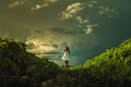 woman wearing white dress standing on hill with green grass under white cloudy sky photo