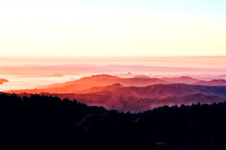 City skyline and a bridge over a river behind undulating hills during sunset photo