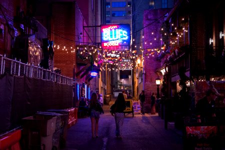 People walking through a downtown street under a line of lights.