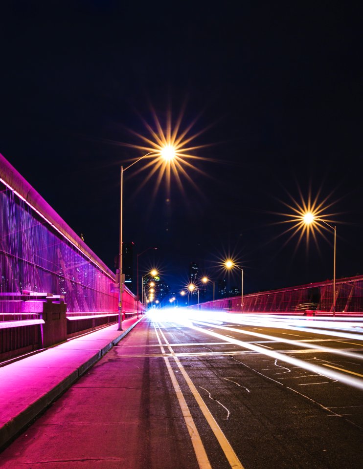 black concrete road between post lamps under black sky at nighttime