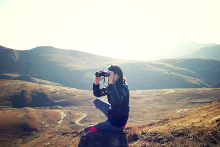 woman wearing black jacket sitting on gray rock and using binoculrs photo