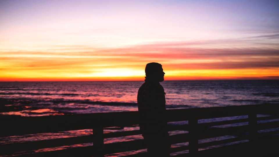 silhouette photo of person standing near body of water photo