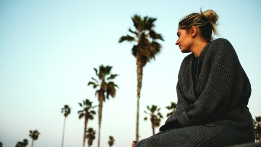 woman wearing gray sweater sitting with the distance of coconut trees under white cloudy sky