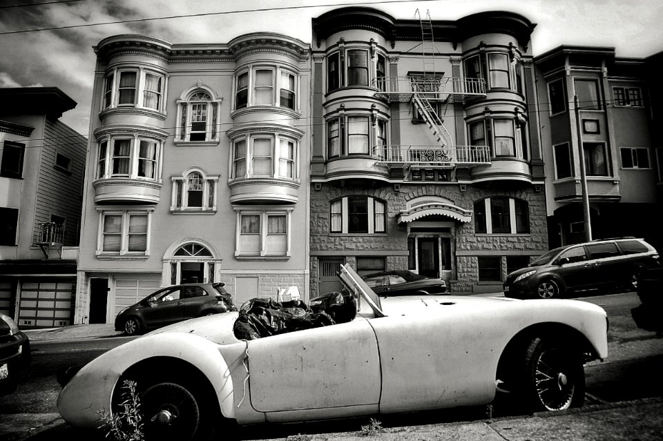 grayscale photo of convertible coupe park near building