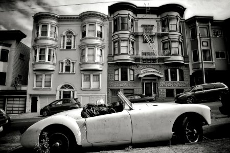 grayscale photo of convertible coupe park near building photo