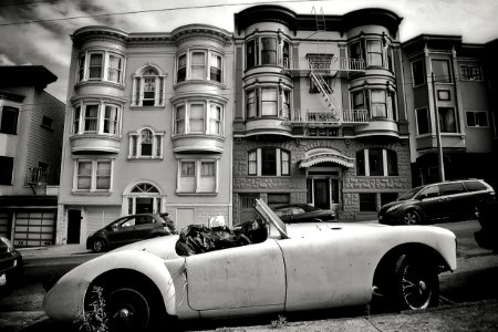 grayscale photo of convertible coupe park near building