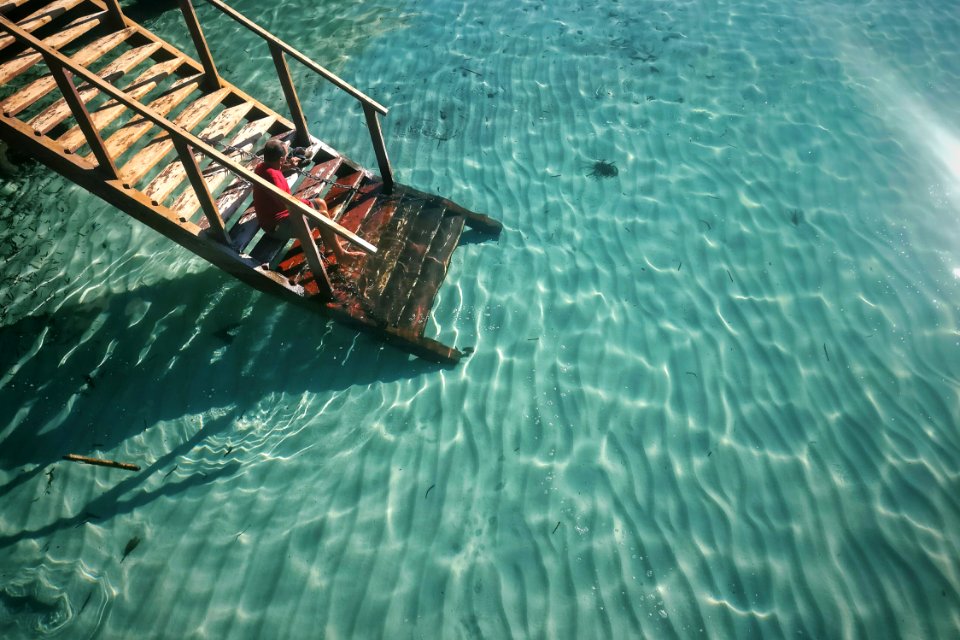 person sitting on brown wooden stairs in front of swimming pool