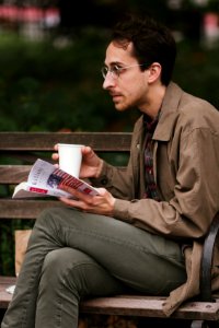 man in brown leather jacket and gray denim jeans sitting on bench reading book photo