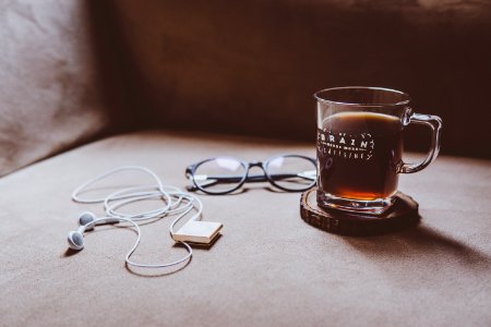 clear Brain printed glass mug on brown wood slab coaster beside black framed eyeglasses and white earphones photo