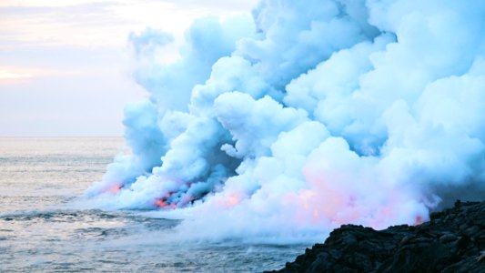 fire and smoke on body of water near rock formation under cloudy sky photo