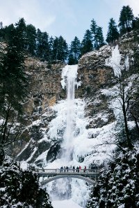 people walking on bridge beside frosted waterfalls during daytime photo