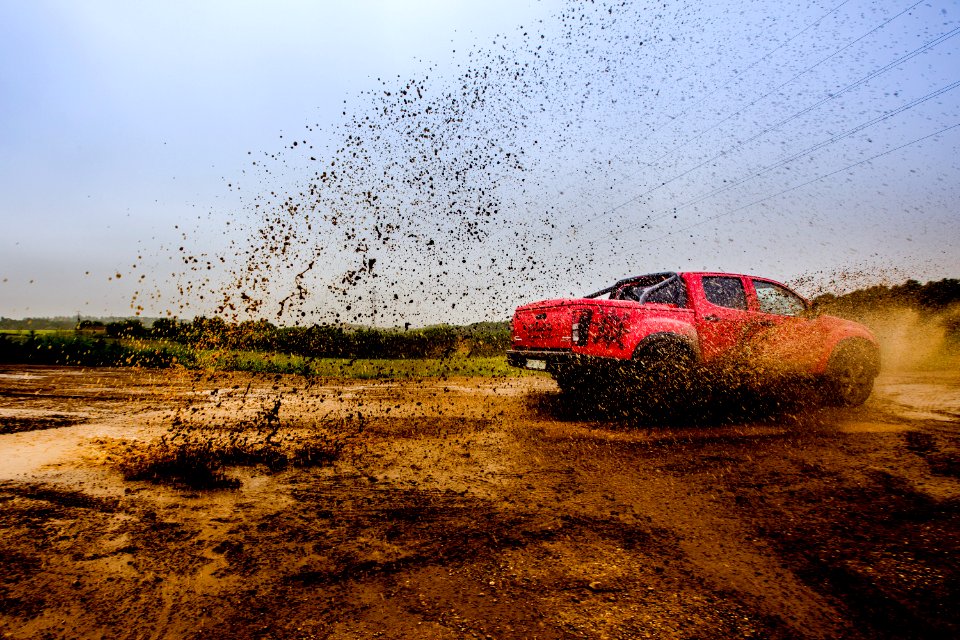 red 4-door truck on mud near trees under cloudy sky