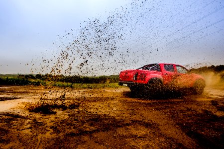 red 4-door truck on mud near trees under cloudy sky