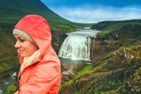 woman wearing pink hoodie standing on top of mountain near waterfalls photo