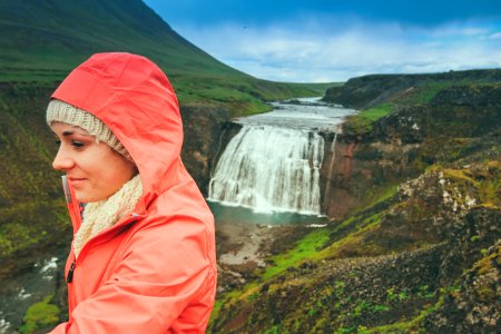 woman wearing pink hoodie standing on top of mountain near waterfalls