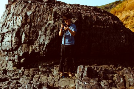 man holding camera while standing on cliff during daytime photo